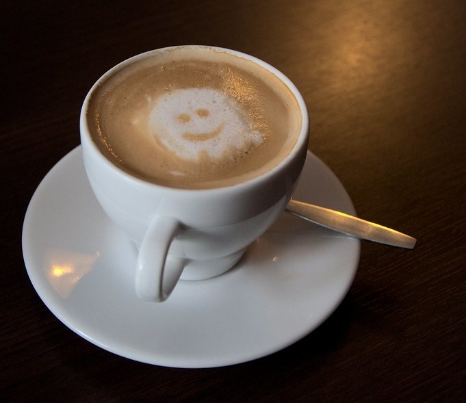 A cup of coffee with a latte art smily face on it